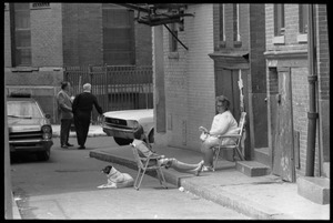 Women and a dog sitting in lawn chairs on a side street in North End, Boston