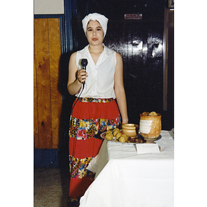 A woman stands next to a table holding a microphone at the Festival Puertorriqueño