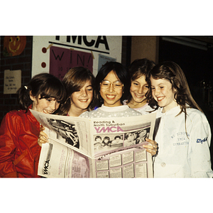 Girls smiling while looking at an issue of the Reading & North Suburban YMCA newsletter