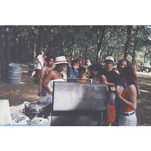 Carmen Pola stands next to the grill with several others at an outdoor picnic event