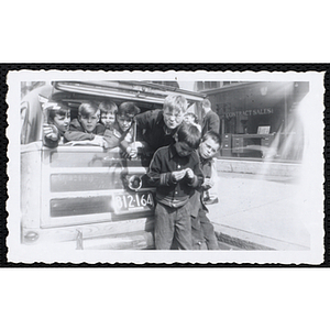 Several Boys' Club members posing in the rear window of a car with "BU Service Day" pennants while two others stand outside