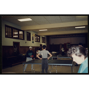 A teenage boy plays table tennis as another teenage boy looks on