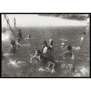 A group of children splash around in the water by a rope line