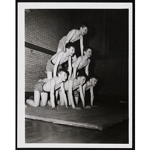 Six boys create a human pyramid in a gymnasium