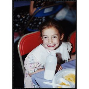 A girl smiles for the camera while sitting at a table with food during a Boys & Girls Club event