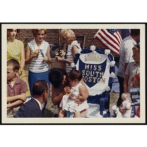 Miss South Boston, the winner of the Boys' Club Little Sister Contest, sits on her mother's lap while the judges look on during the award ceremony