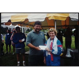 A woman and a man pose with envelope as Charlestown director Jerry Steimel (background, left) looks on during the Battle of Bunker Hill Road Race