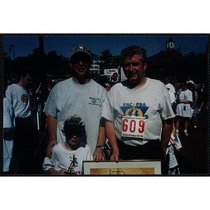Executive Director Jerry Steimel (upper left), a man, and a boy pose with framed print at the Battle of Bunker Hill Road Race
