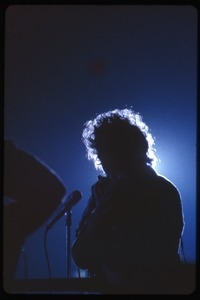Bob Dylan performing on stage, silhouetted in blue
