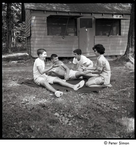 Camp Arcadia: campers seated on a blanket in front of a cabin