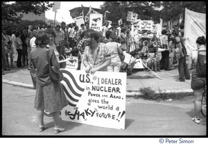 Antinuclear protester with sign reading 'U.S. #1 dealer in nuclear power and arms gives the world a shaky future' and crowd of protesters behind