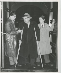 Two young men assisting a man on crutches as he exits a building