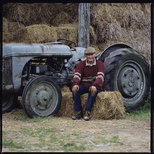 Robin Matthews sitting on hay bale with his tractor behind him