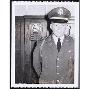 A man in a uniform stands in front of a plaque on the wall