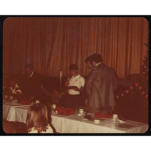 A boy speaks into a microphone at a Christmas party as two men look on