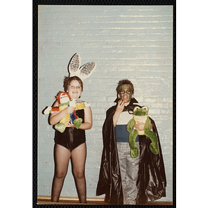 A boy and a girl pose in their Halloween costumes in front of a blue brick wall