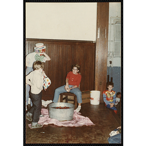 Children in Halloween costumes gather around a basin filled with water and apples for bobbing