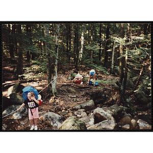 Two girls with backpacks stop along the Piper Trail near a girl crossing the creek