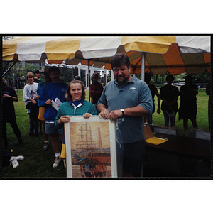 A girl and a man pose with a framed print as Executive Director Jerry Steimel (background, left) looks on during the Battle of Bunker Hill Road Race