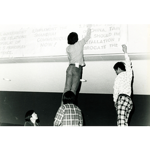 Two men hang a banner in the Josiah Quincy School auditorium in preparation for an event about the normalization of U.S. and China relations