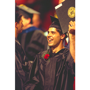 A smiling graduate holds up his diploma during the commencement ceremony