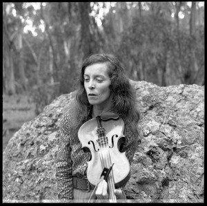 Woman posed with a fiddle, seated on a granite boulder in a eucalyptus grove