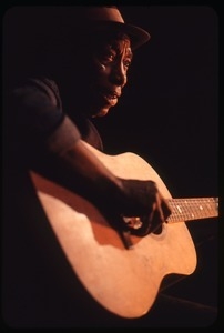 Mississippi John Hurt: studio portrait, seated, playing guitar