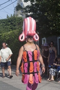 Marcher with large headress and flip-flop dress, along side the parade float for Priscilla, Queen of the Cape : Provincetown Carnival parade