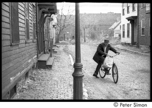 Older man riding a bicycle down a rough Roxbury street