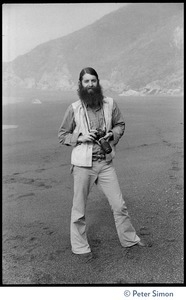 Rameshwar Das: full-length portrait with camera, standing on the beach