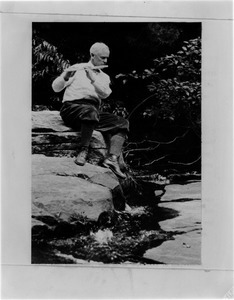 Frank A. Waugh sitting on a rock playing a flute