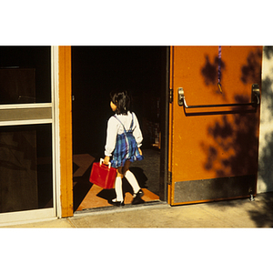 Child carrying red lunchbox walking into school