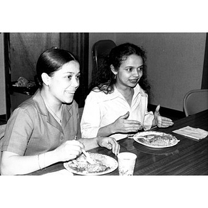 Two young women with plates of food at a community gathering.