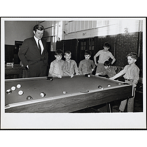 Senator Ted Kennedy stands at a billiard table with six Boys' Club members as one of them shoots pool