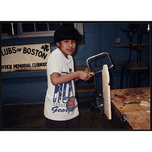 A boy using a hacksaw for his woodworking project at the South Boston Boys and Girls Club