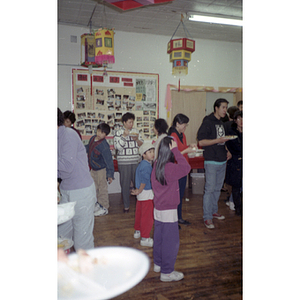 Adults and children stand with plates of food at the Chinese Progressive Association's office for a celebration of the Chinese New Year
