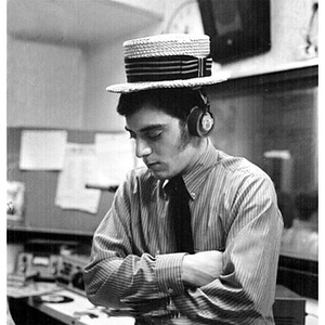 Young man in a straw hat and headphones standing in the broadcast booth at the WNEU studio
