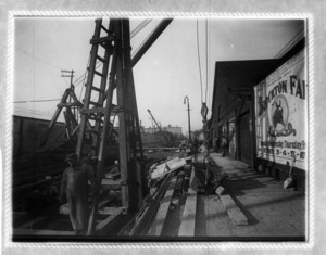 Construction site, including workers and a crane, in front of a billboard for Brockton Farm
