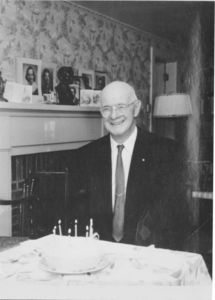 Gleason L. Archer (President, 1937-1948, and Founder of Suffolk University) in front of birthday cake at his 79th birthday party, 3rd floor living room, Suffolk Law School