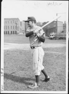Suffolk University's baseball coach George Doucet swings a bat, 1961
