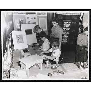 An art instructor watches three boys working on their projects in the "Boys' Clubs of Boston booth at Do-It-Yourself Show at Mechanics Building, Boston Nov. 25, 1957"