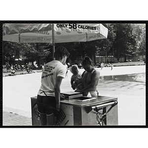 A teenage boy operating an ice juice cart waits on a woman with an infant on Boston Common