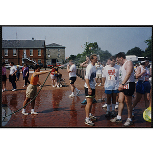 A woman cools runners with water from a hose during the Bunker Hill Road Race
