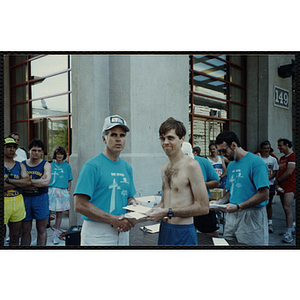 A man receives a certificate from another man as he shakes his hand during the Battle of Bunker Hill Road Race