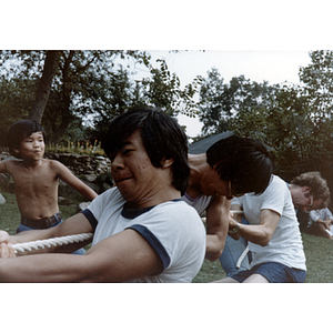 Four young men play tug-of-war, while a young boy watches in the background