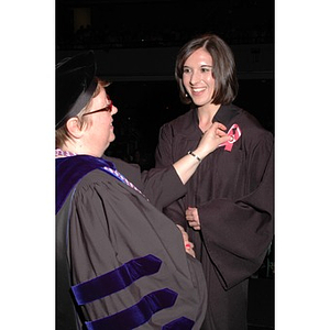 School of Nursing faculty member pins a pin and ribbon to a student's graduation robe at pinning ceremony during convocation