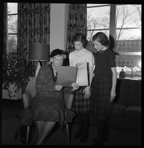 Eleanor Roosevelt (center) seated in the Cape Cod Lounge (Student Union), reading a book report presented by two young girls, during Roosevelt's Distinguished Visitors Program appearance at UMass Amherst
