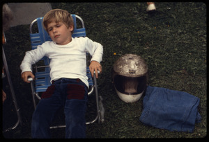 Young boy in a folding lawn chair with motorcycle helmet