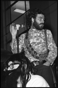 Jerry Rubin, with bandolier and toy assault rifle slung over his shoulder, addressing the audience at the microphone