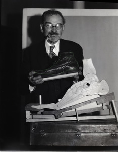 Carl Krippendorf, smoking a shoe and holding a shoe in front of a model of a foot
